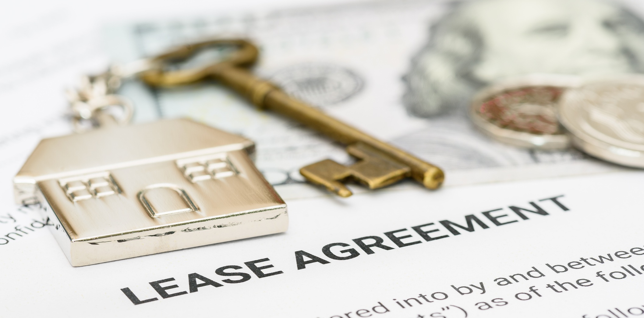 Property rental, leasing contracts, real estate, housing agreements, and property management. A close-up view of a lease agreement document with a house key, coins, US dollar, and a pen placed on top.